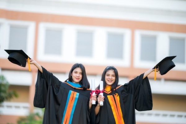 portrait-two-female-graduates-university-graduates-happily-holding-their-hats-up-front_43157-1258